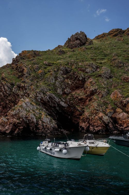 Free Two boats anchored near a rocky cliff with clear blue water and a bright sky. Stock Photo
