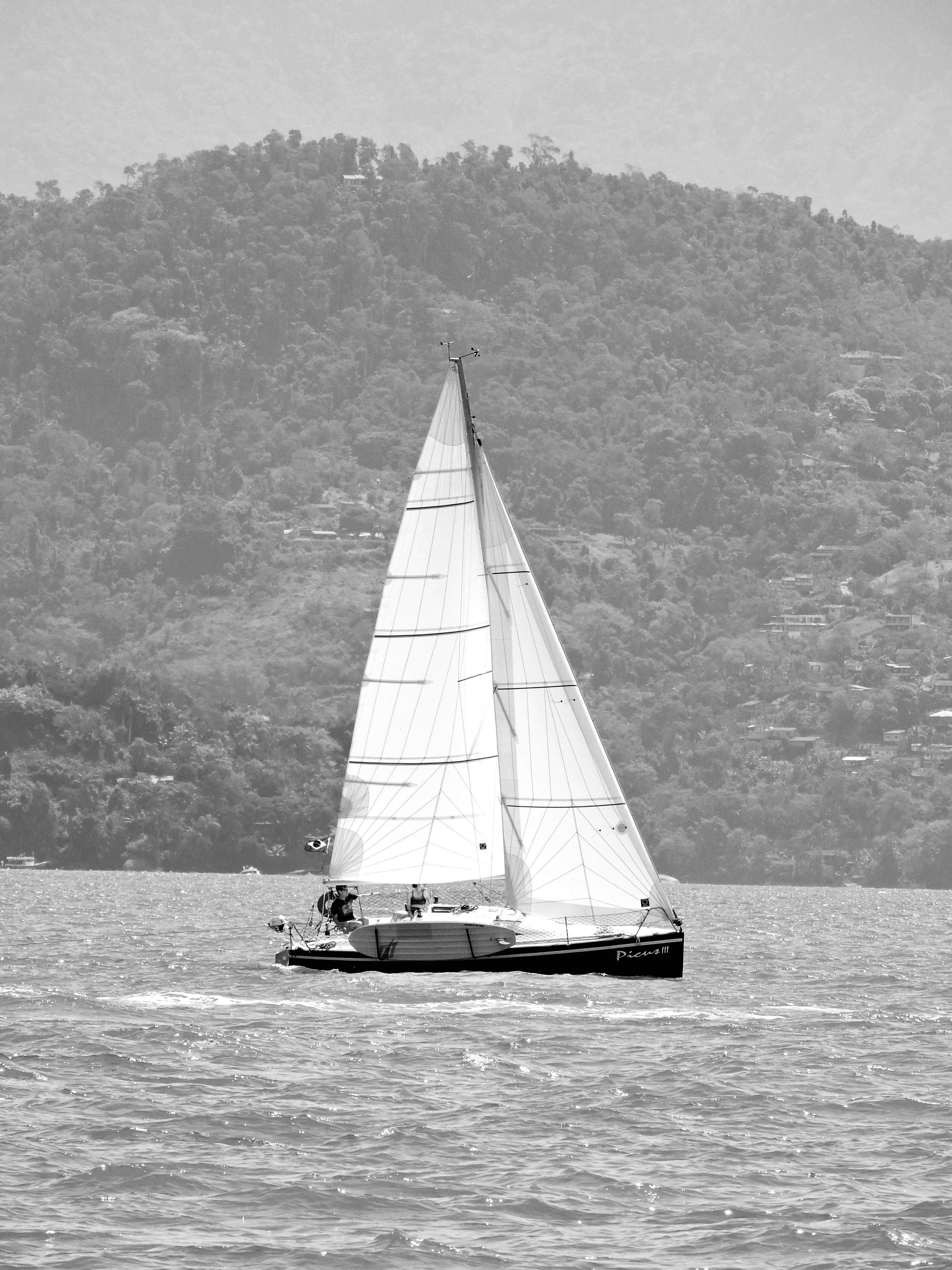 Sailboat with full sails cruising on tranquil waves with forested mountain backdrop.