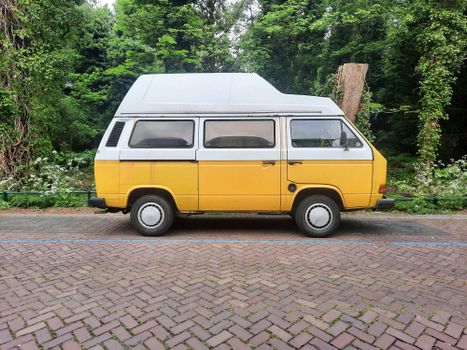 A classic yellow camper van parked by a lush, green park setting, exuding a retro travel vibe.