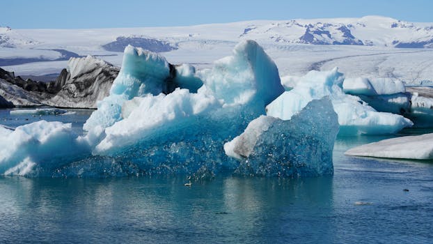 Majestic icebergs floating in an Icelandic glacial lagoon against a backdrop of snow-covered mountains.