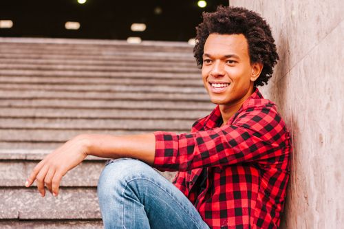 Free Young man in a casual outfit smiling while sitting on outdoor steps. Stock Photo