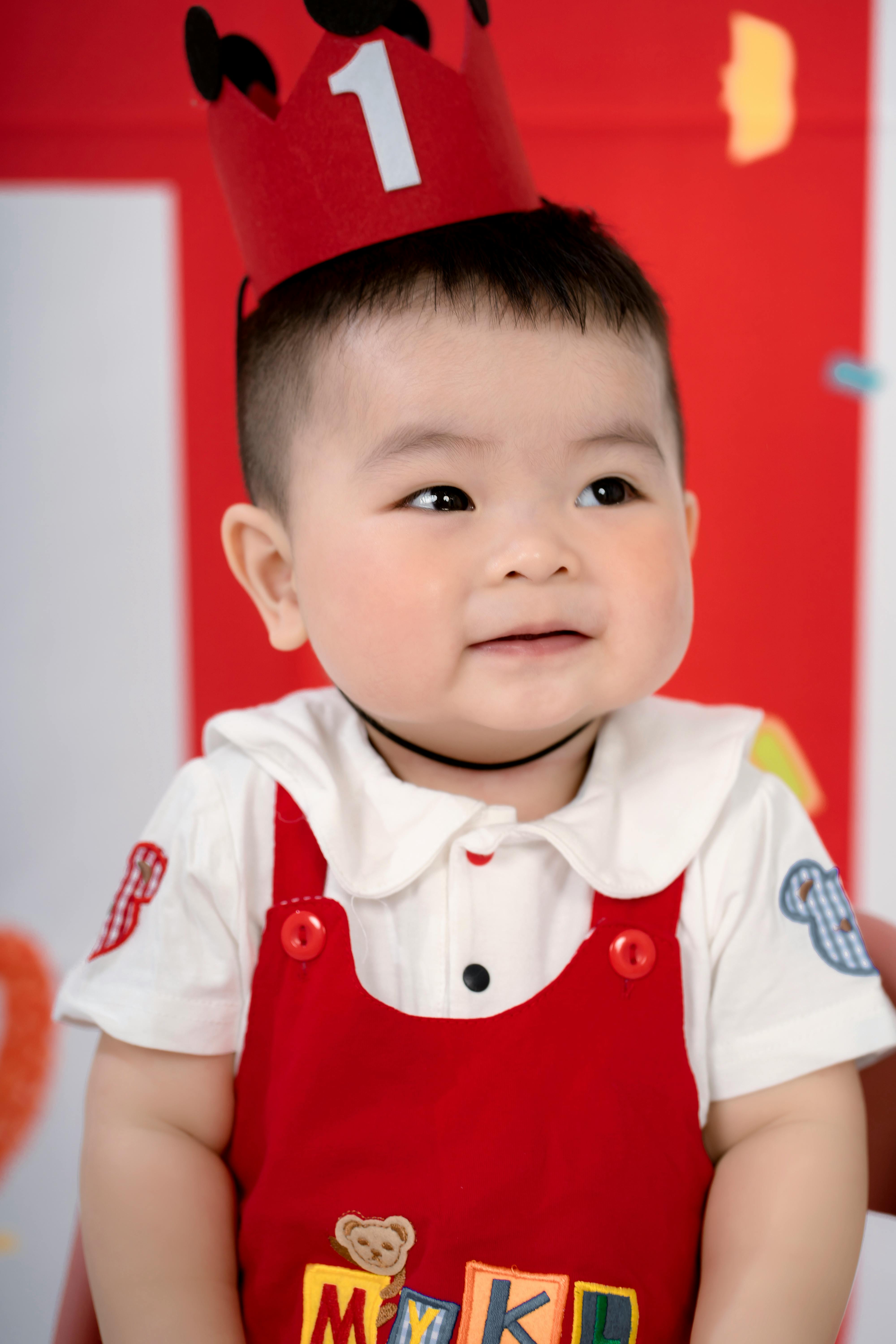 Cute baby in a birthday party setting with colorful decorations wearing a red outfit.