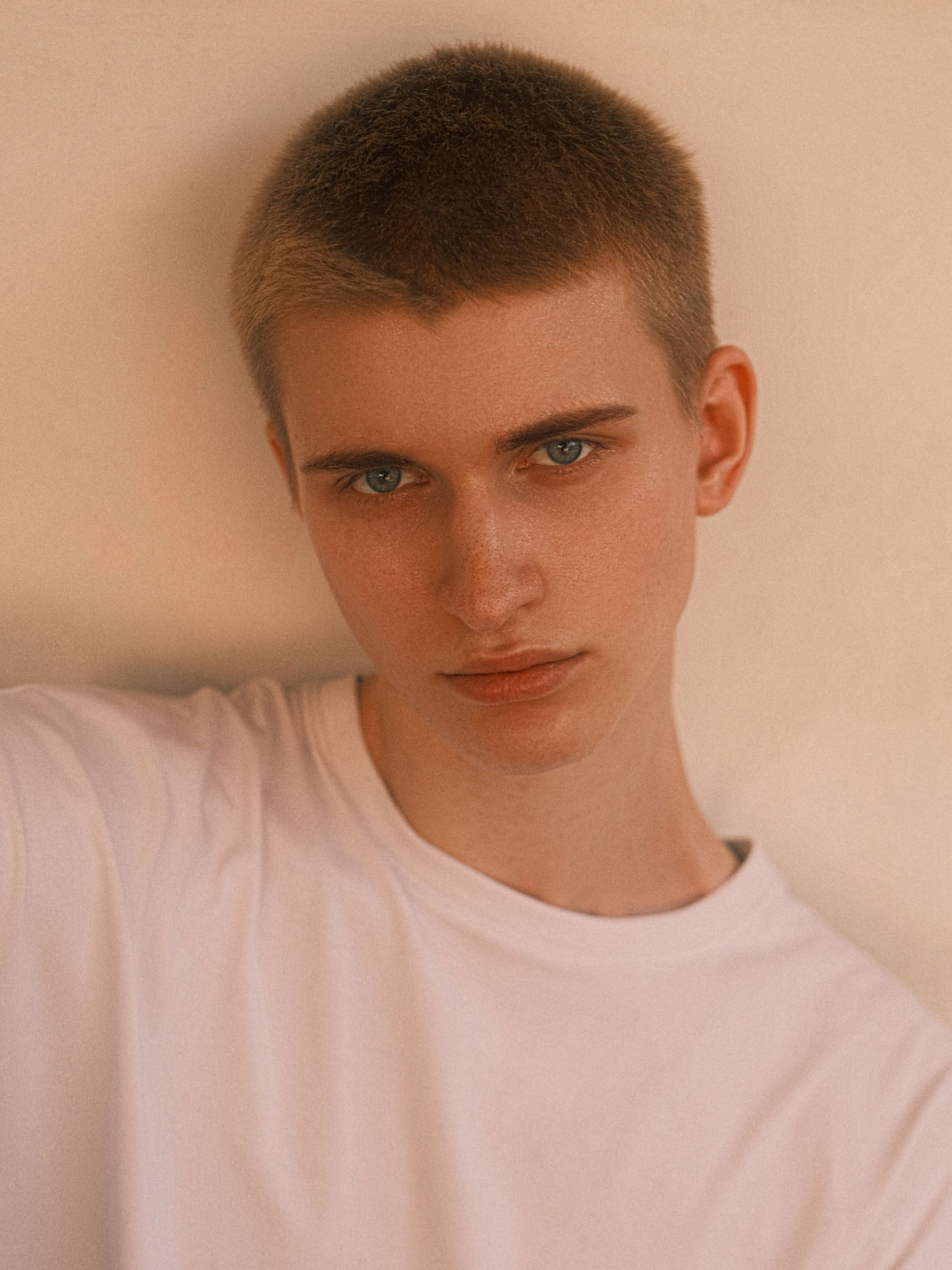 Close-up of young man in a white shirt with neutral expression against a plain background.