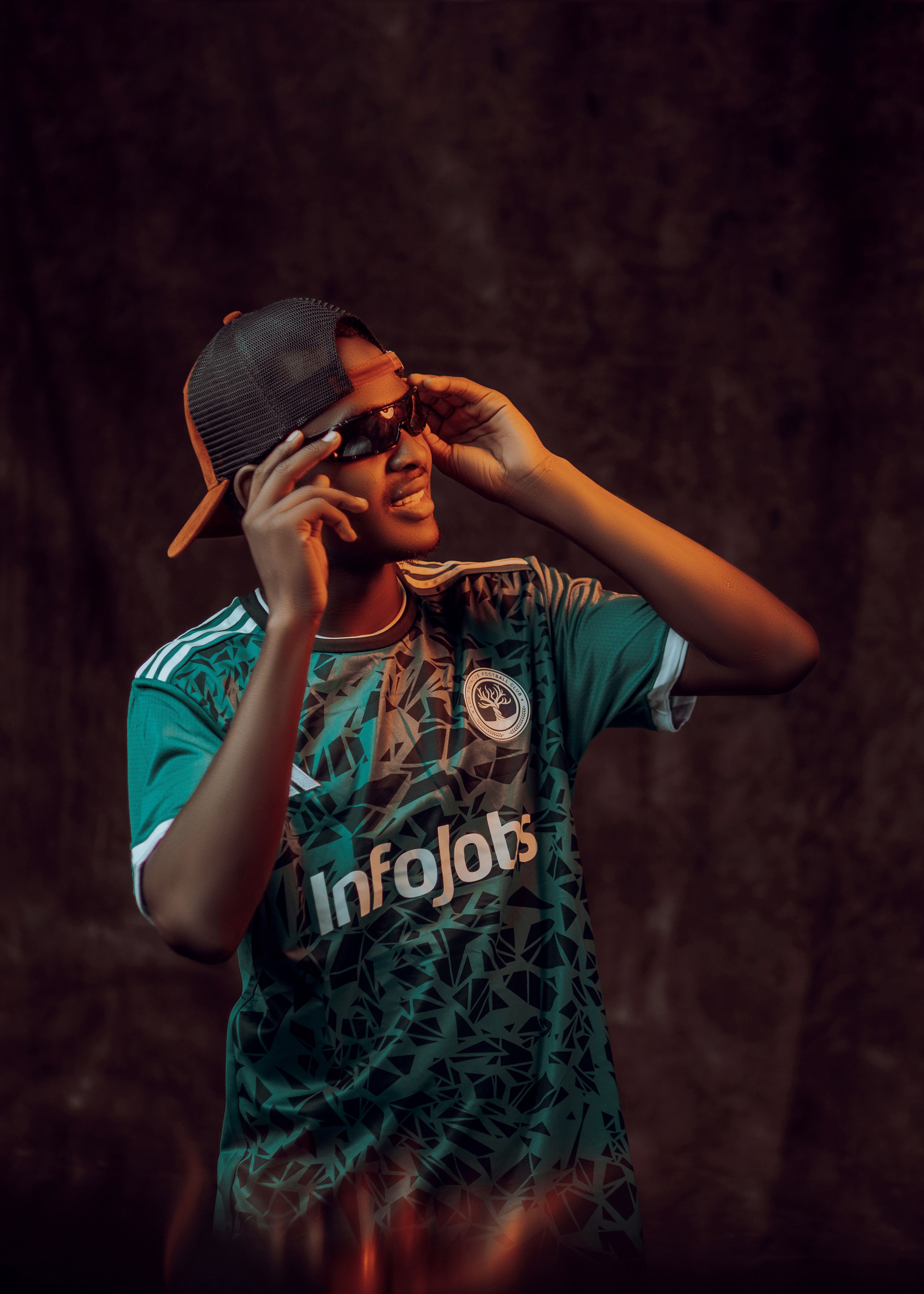 Confident young adult wearing trendy clothing, sunglasses, and cap in a relaxed pose.