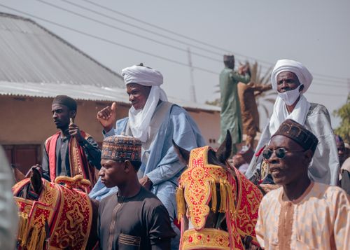 Free Men in traditional attire participating in a cultural parade with colorful horses outdoors during the day. Stock Photo