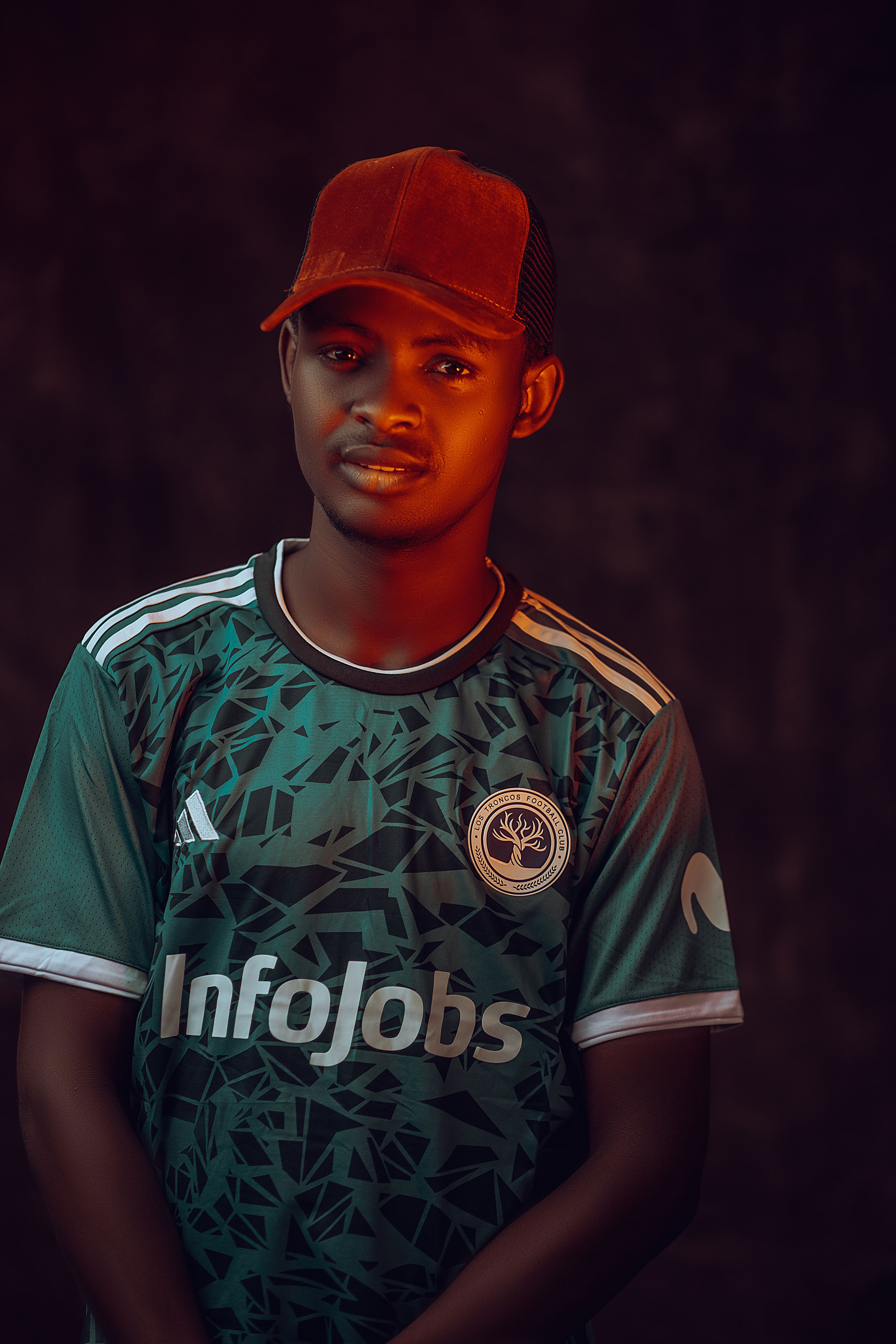 A young man in a green sports jersey and cap posing against a dark background.