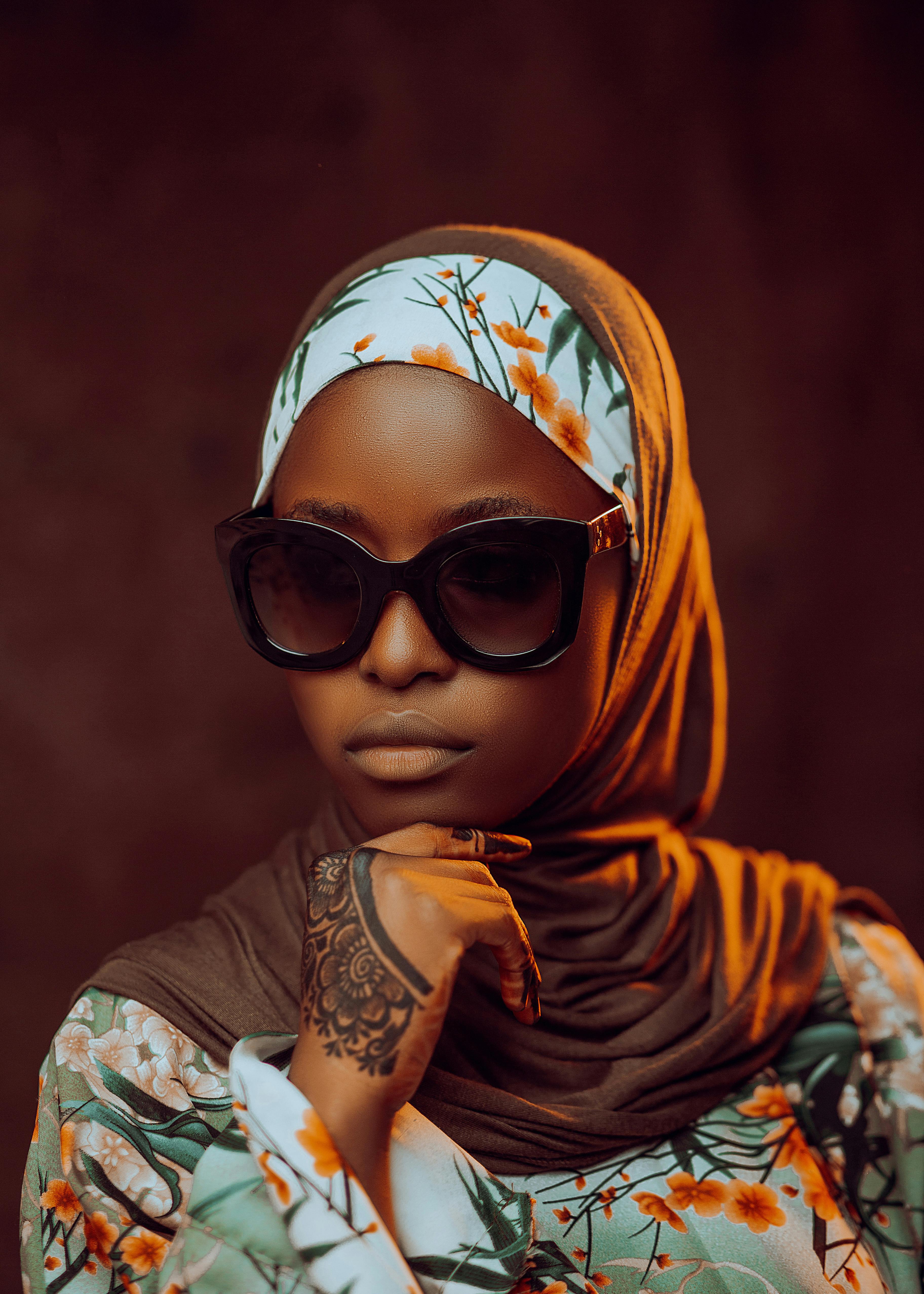 Stylish woman wearing sunglasses, floral headscarf, and intricate henna tattoo on hand.