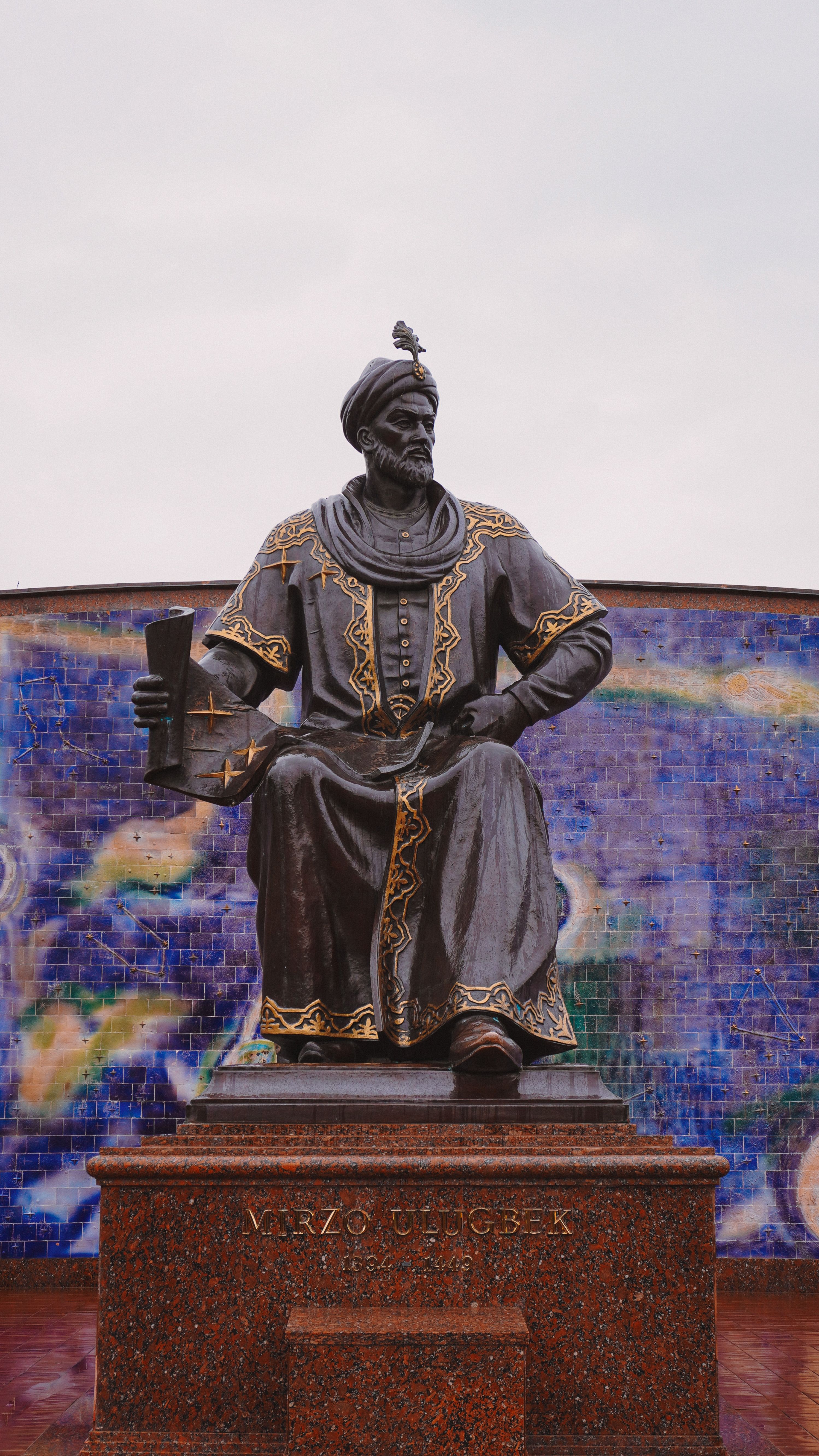 Elegant statue of Ulugh Beg in Samarkand, Uzbekistan, set against a vibrant mosaic backdrop.