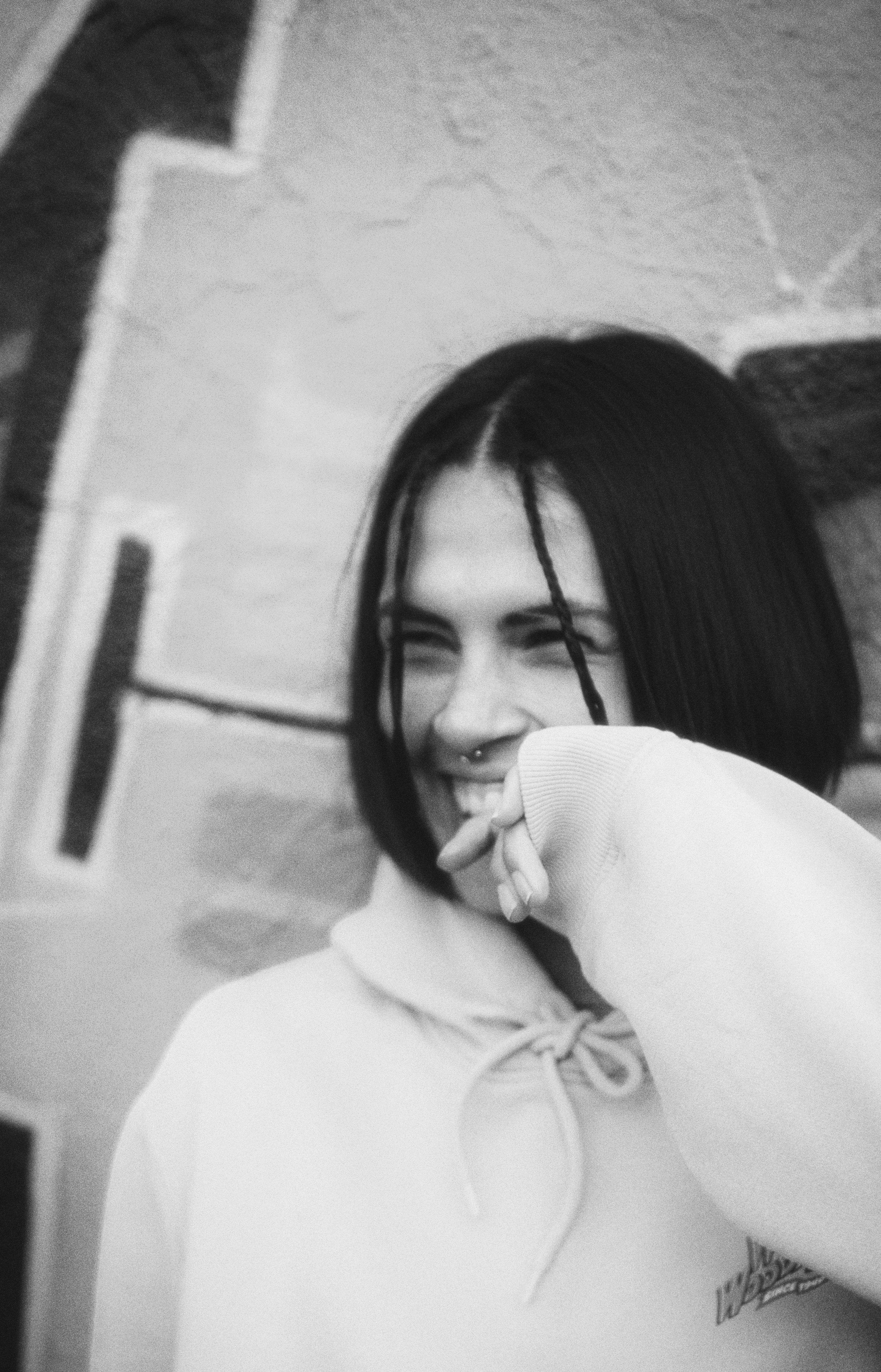 Black and white portrait of a woman laughing against a graffiti wall.