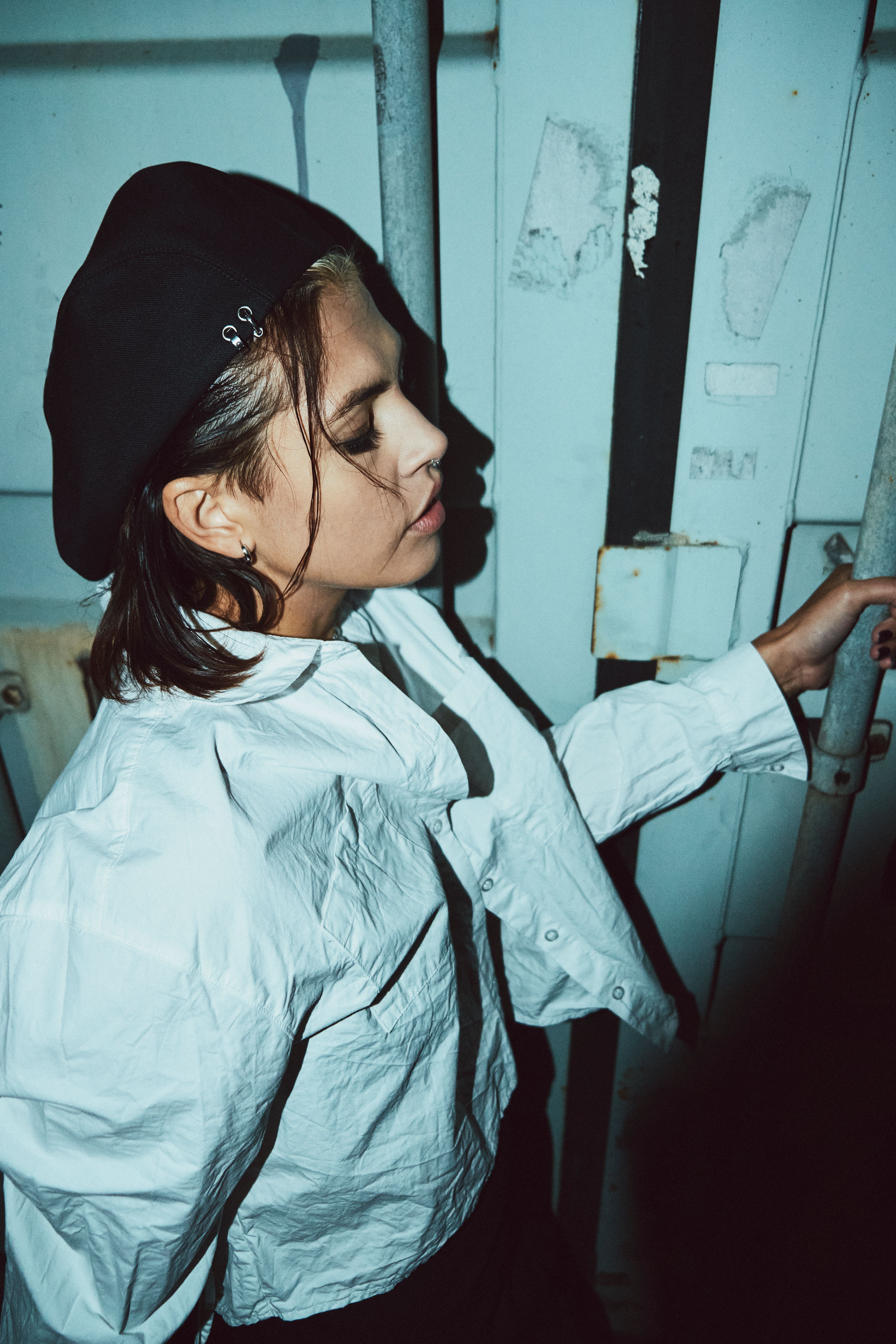 Woman in beret and white shirt posing against a textured wall in an industrial setting.