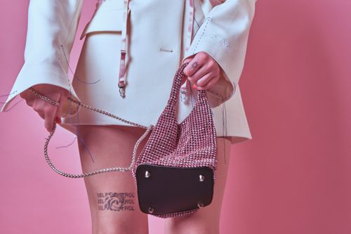 Free Fashion-forward image of a woman in white attire holding a pink bejeweled handbag against a pink background. Stock Photo