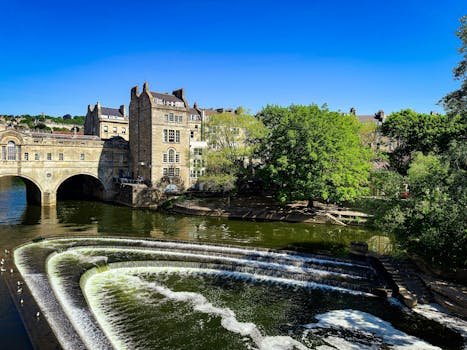 Scenic view of Pulteney Bridge over the River Avon in Bath, England, under a clear blue sky.
