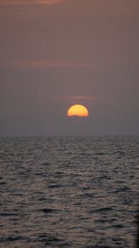 A stunning view of the sun setting over a calm ocean, creating a peaceful ambiance.