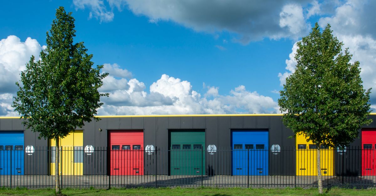 Vibrant garage doors in different colors with bright sky and clouds above, enclosed by iron gates.