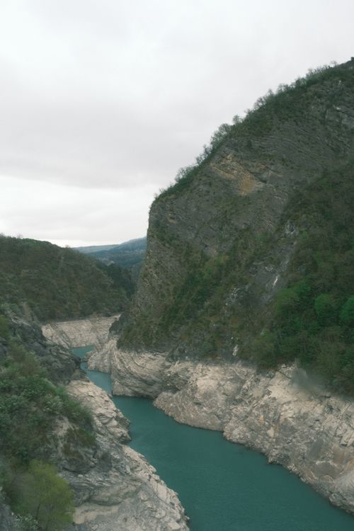 Free A tranquil river winding through a rugged canyon with lush greenery and rocky cliffs under an overcast sky. Stock Photo