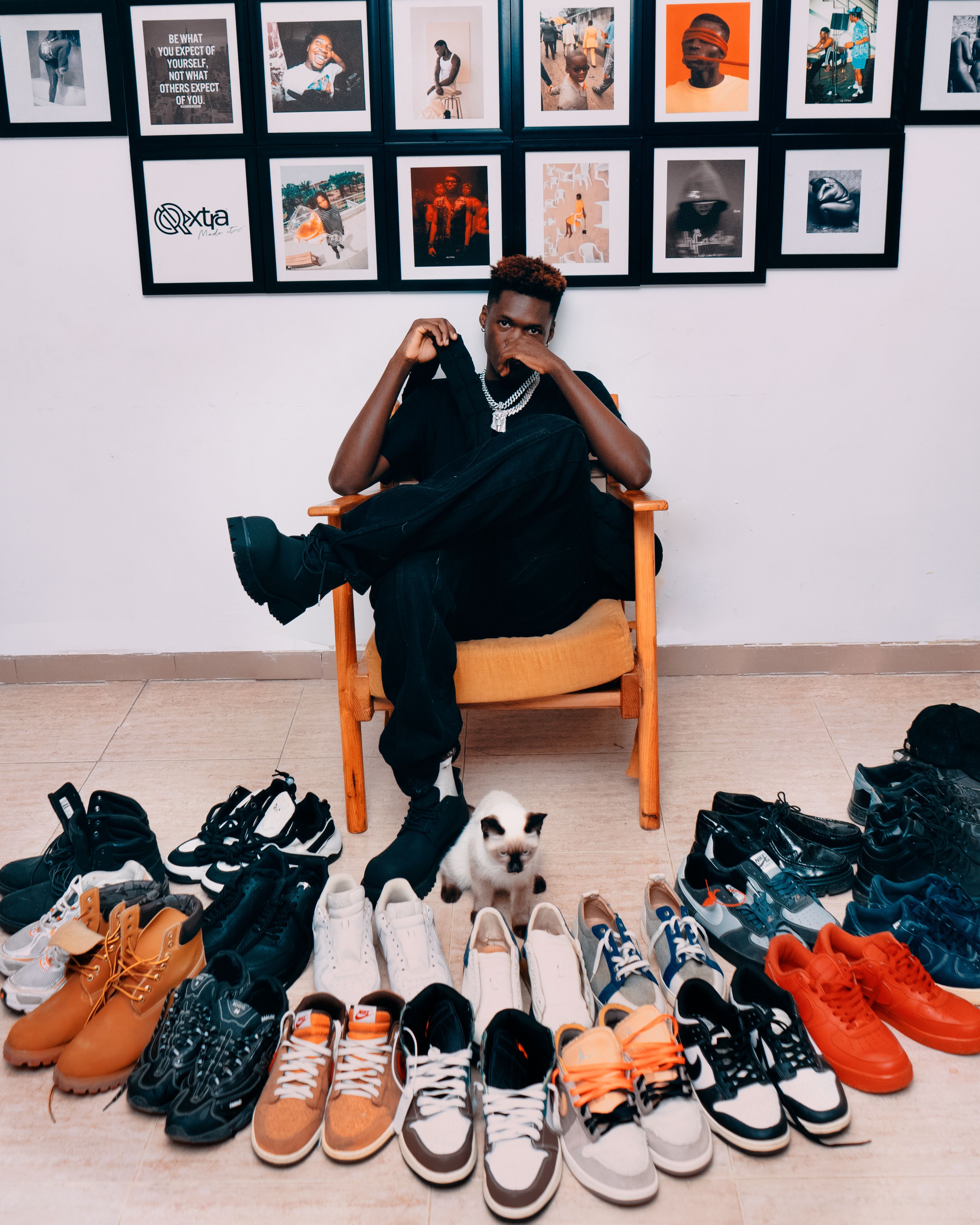 Man sitting with a cat surrounded by a diverse sneaker collection, indoors.