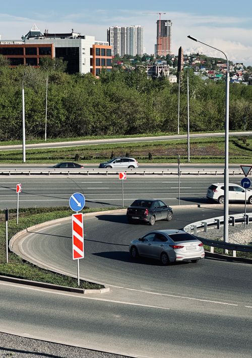 Free Cars navigating roundabouts and highways with cityscape background. Stock Photo