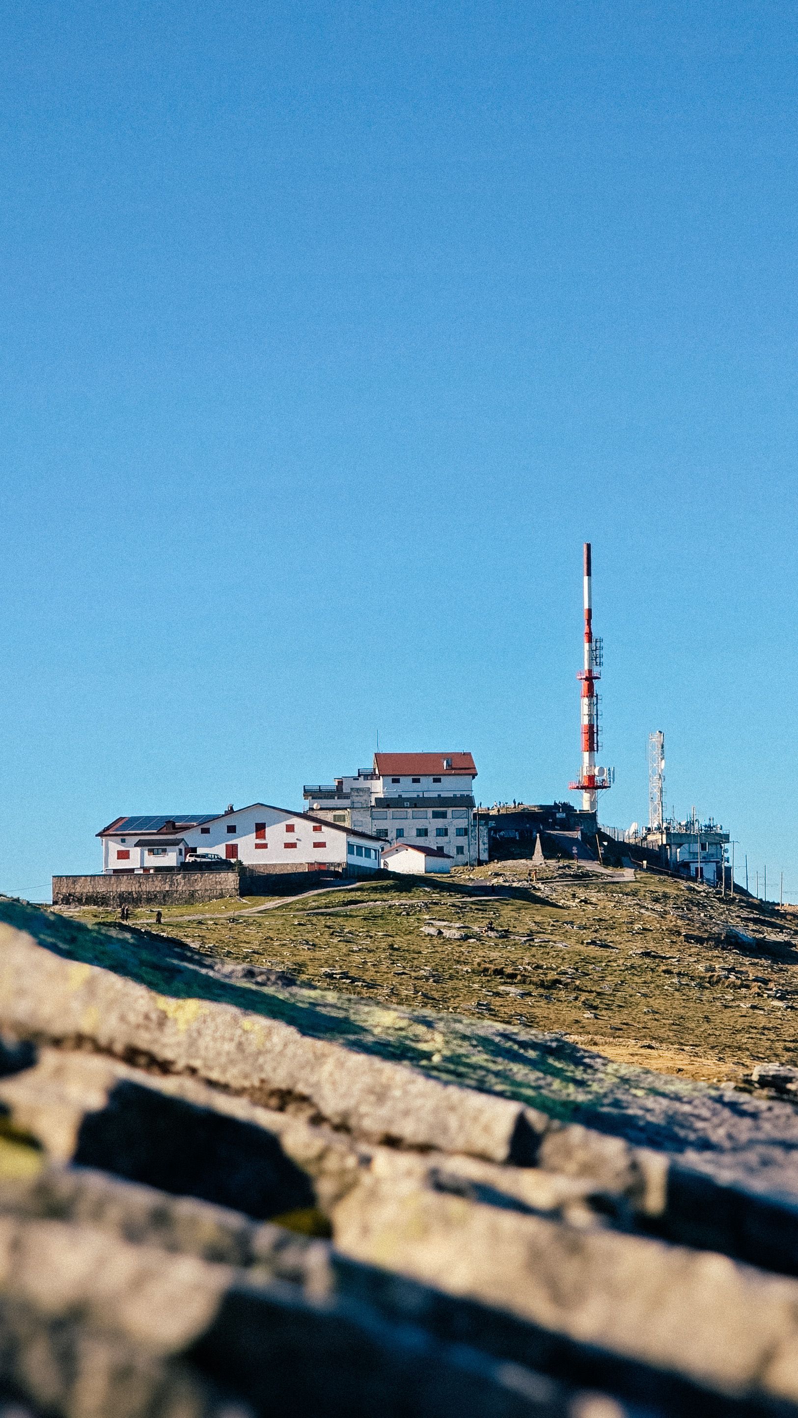Telecommunication tower and buildings on a mountain summit in Ascain, France under clear blue skies.