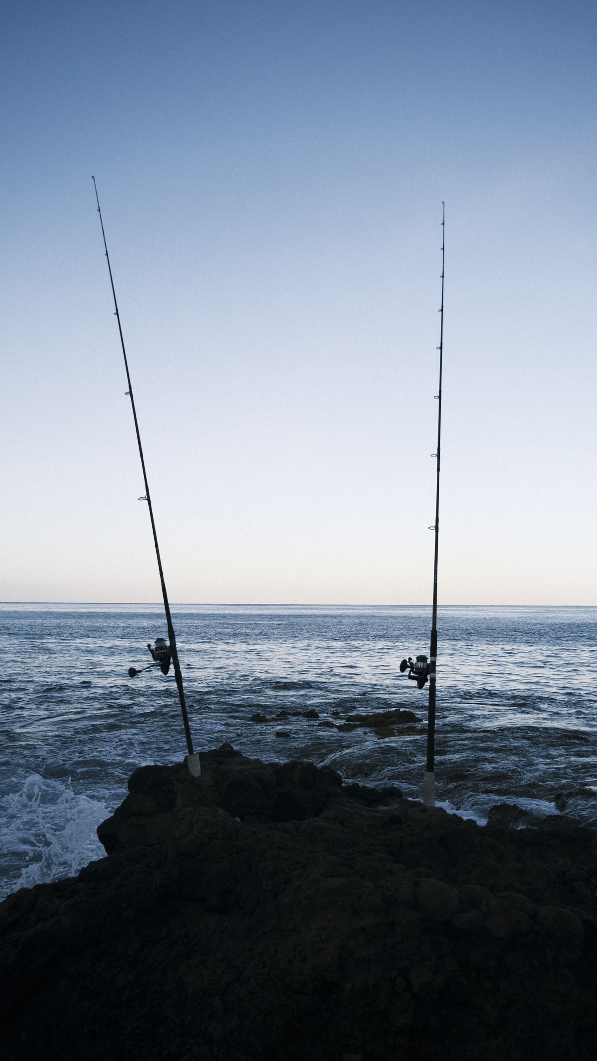 Two fishing rods standing on a rocky shoreline against a calm sea