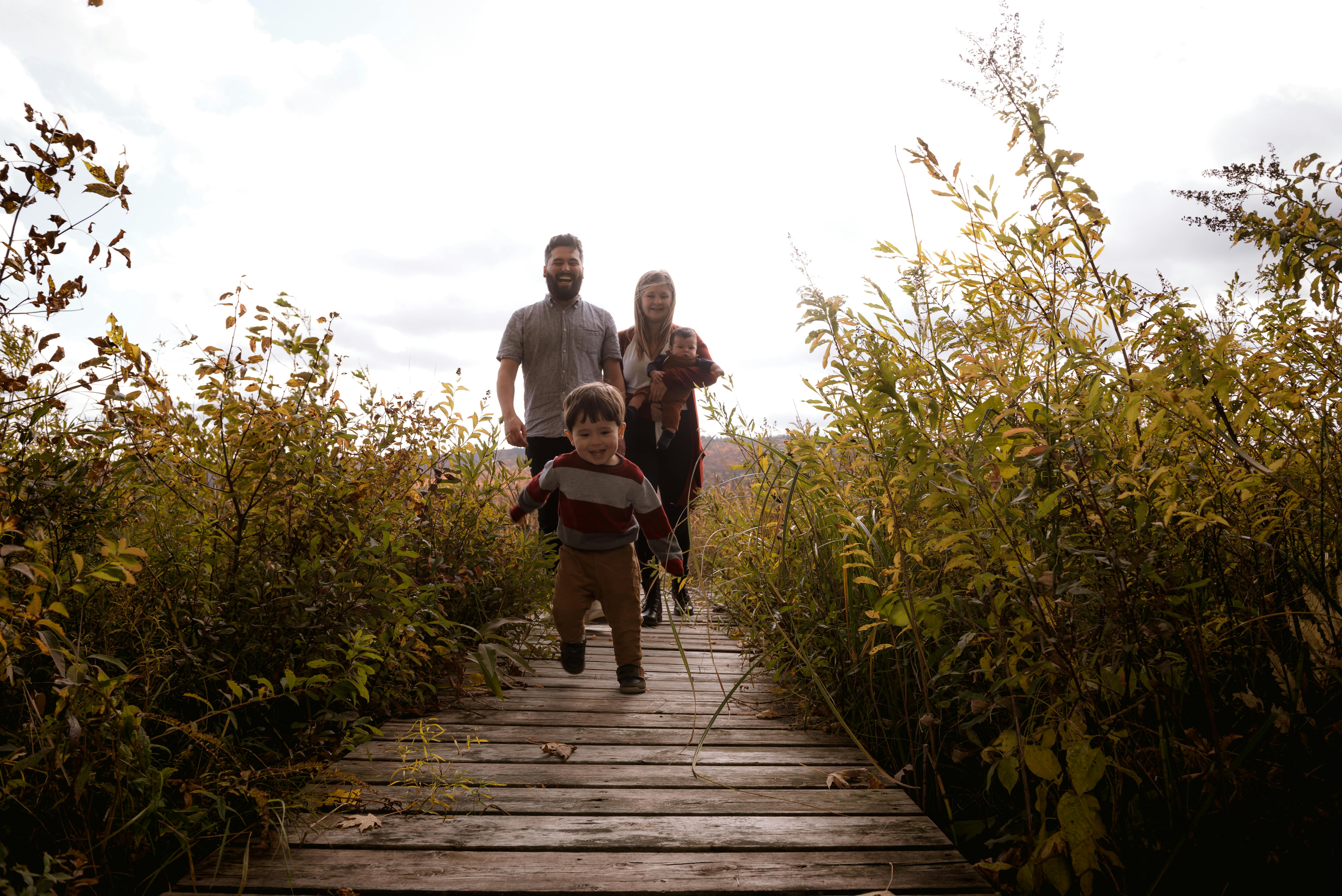 一个快乐的家庭走在秋天绿树环绕的木制小径上