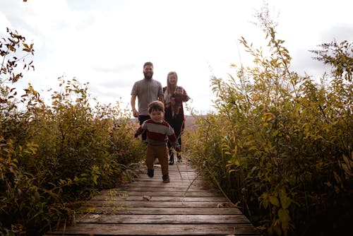 Boy Running on Bridge Near His Parents