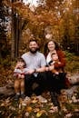 一家人微笑着坐在森林里的一根木头上，周围是秋叶
