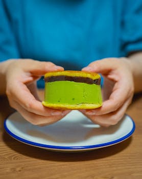 Close-up of matcha dorayaki held by hands over a white plate, showcasing its vibrant color and texture.