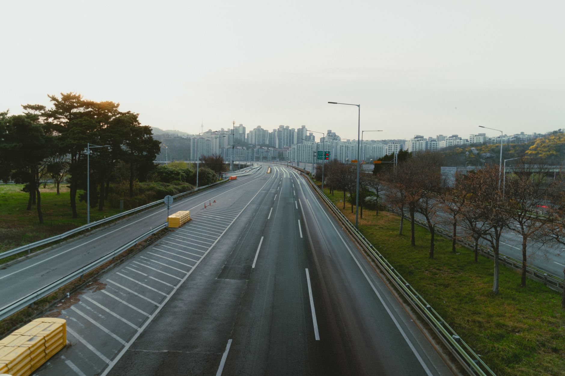 Peaceful view of an empty highway leading to Seoul city skyline with surrounding trees.
