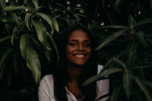 A Woman Smiling Between Dark Green Plants