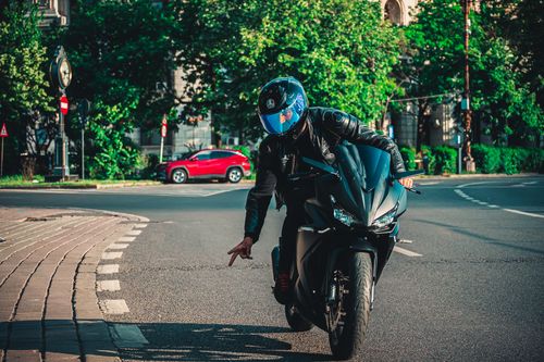 Free A motorcyclist performs a trick on an urban road wearing a helmet and leather jacket. Stock Photo