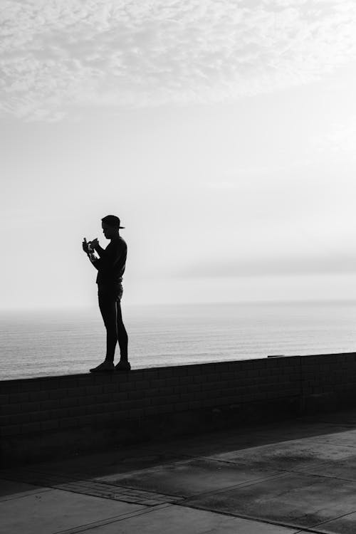 Monochrome Photo of Person Standing Near Seashore