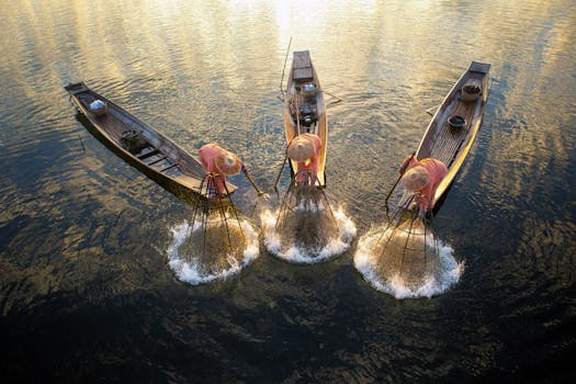 Fishermen with nets on wooden boats during a golden sunrise in Shan, Myanmar.