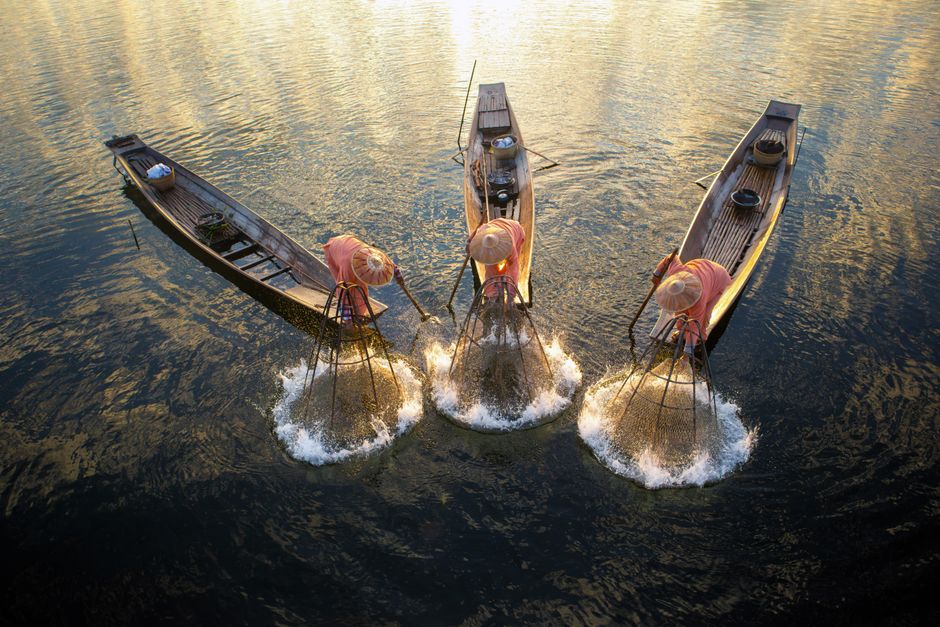 Fishermen with nets on wooden boats during a golden sunrise in Shan, Myanmar.