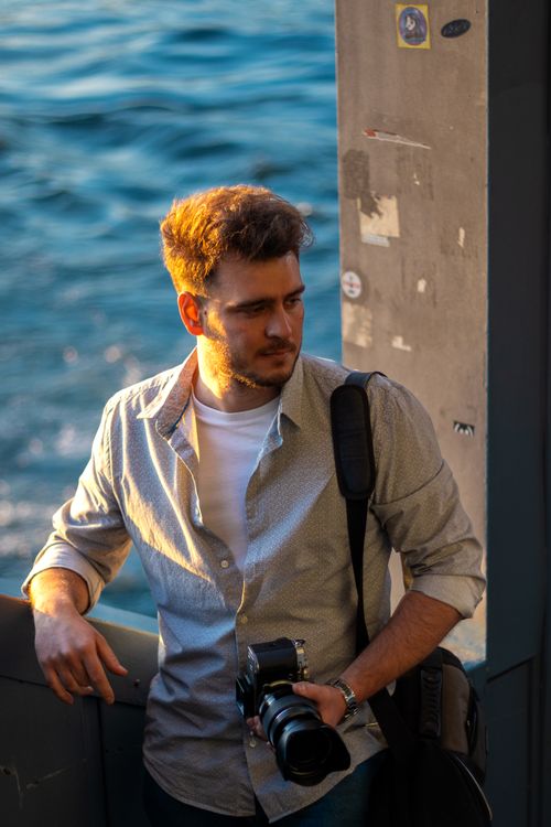 Free A young photographer stands by the Bosphorus in İstanbul during sunset, capturing the golden hour glow. Stock Photo