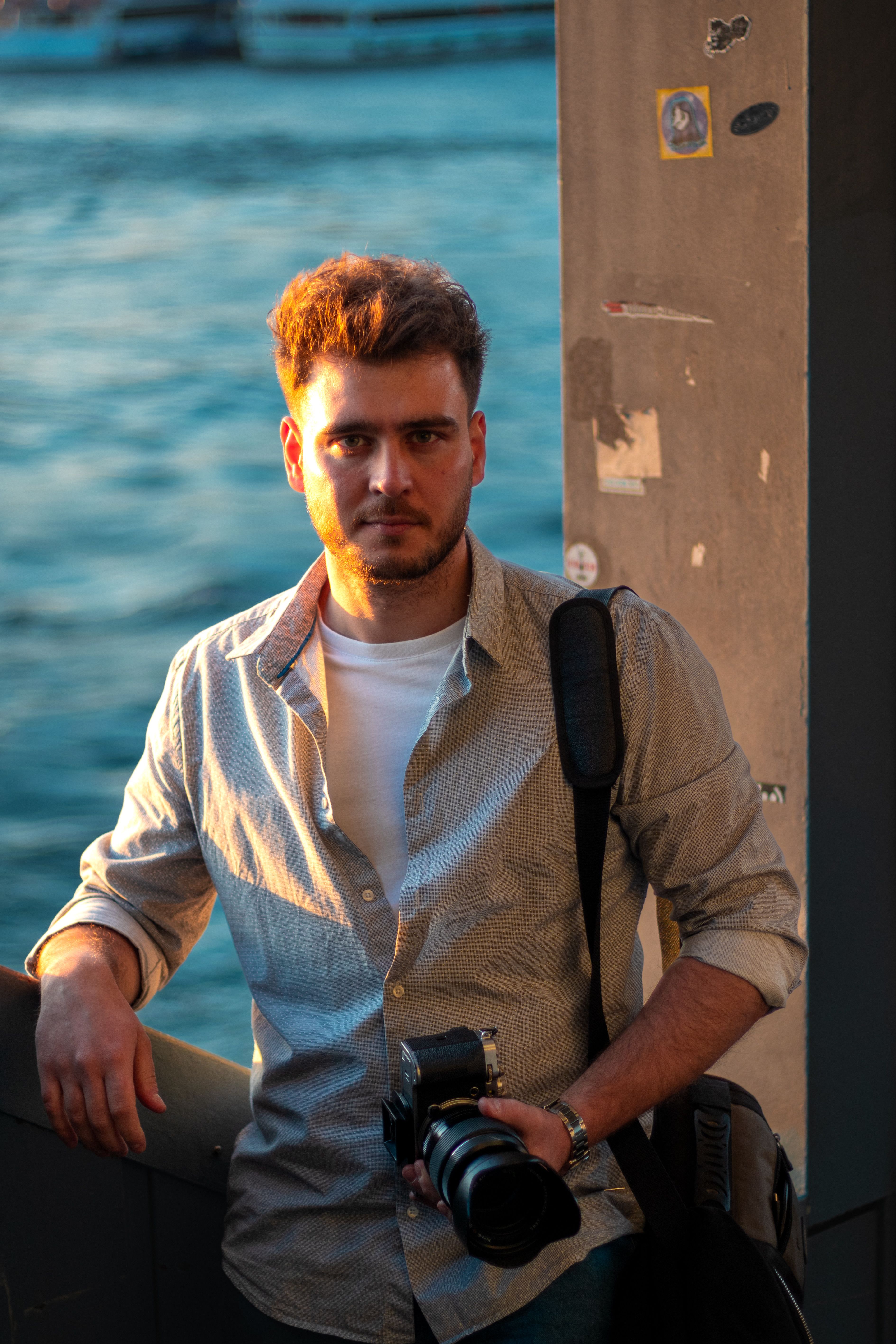 A photographer standing by the water in Istanbul, holding a camera at sunset.