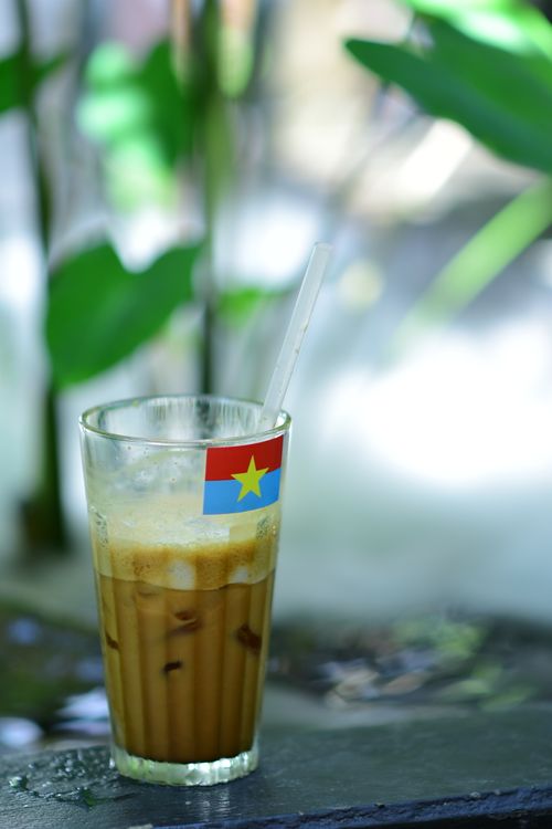 Free Refreshing iced coffee with a colorful flag adorns a clear glass, set outdoors with natural backdrop. Stock Photo