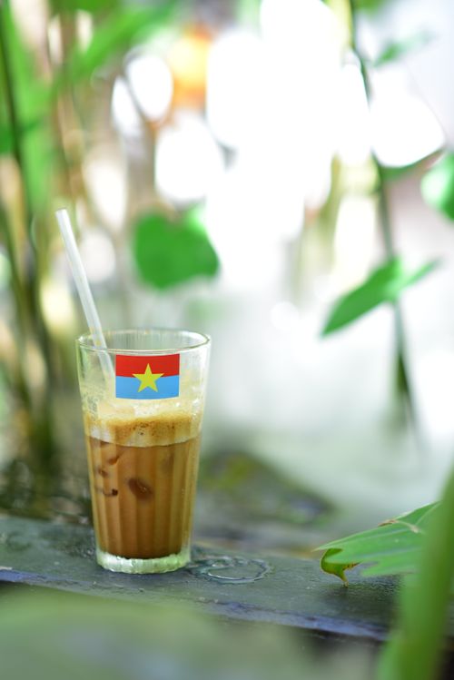 Free Close-up of a Vietnamese iced coffee outdoors with a straw and flag, surrounded by greenery. Stock Photo