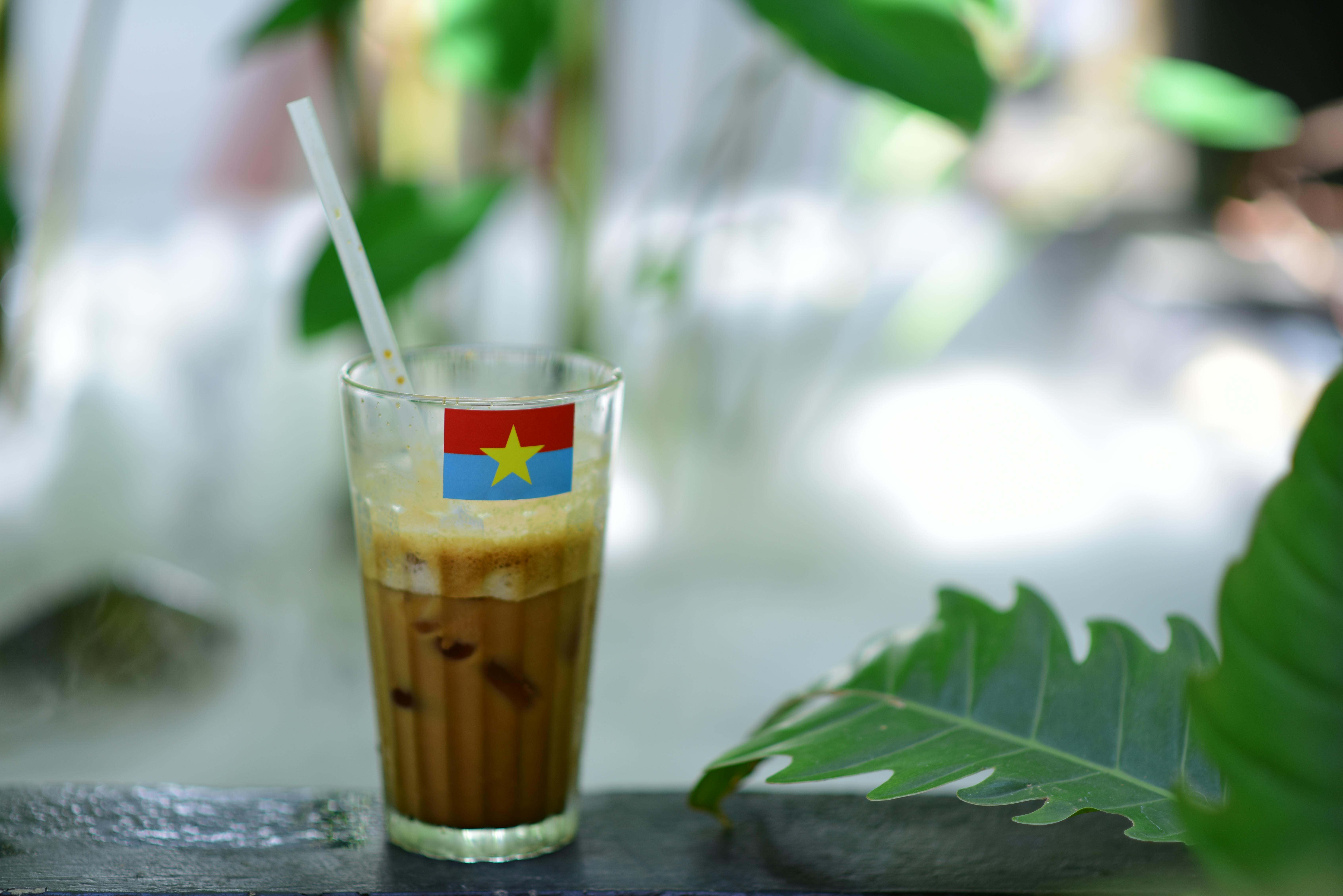 A glass of Vietnamese iced coffee with a straw, adorned with a flag label, amidst lush greenery.