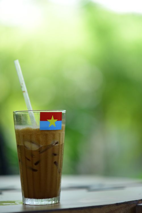 Free Iced coffee in a glass with a Vietnamese flag stirrer against green blurred background. Stock Photo