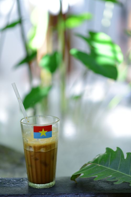 Free Refreshing iced coffee with straw and flag, set against lush tropical plants. Stock Photo