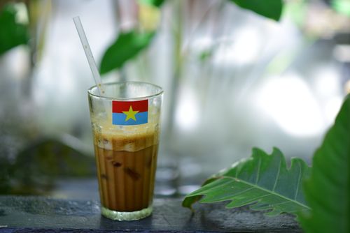 Free Glass of iced coffee adorned with Vietnamese flag outdoors with greenery. Stock Photo
