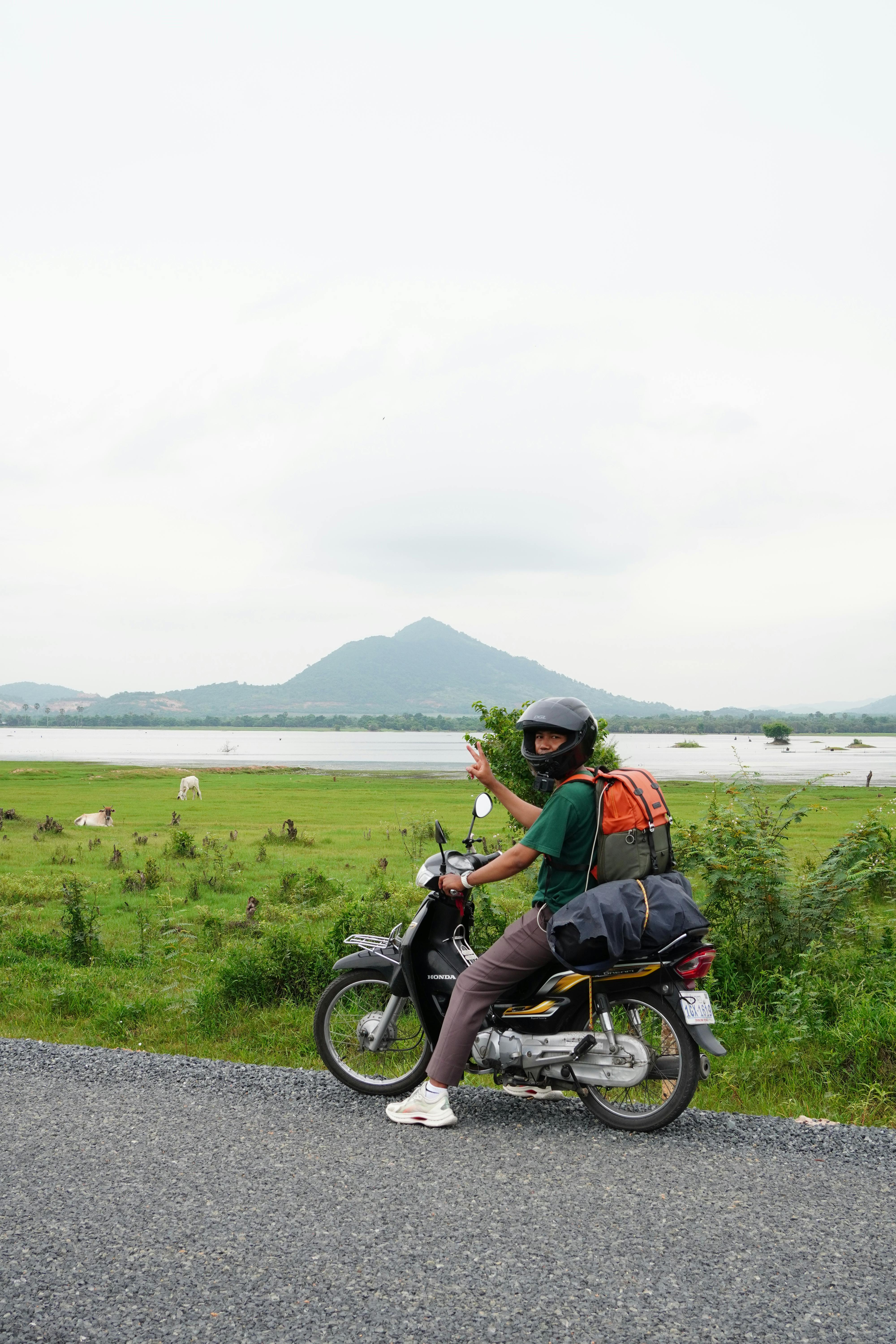A person on a motorcycle exploring the beautiful countryside of Kampot, Cambodia with mountains in the background.