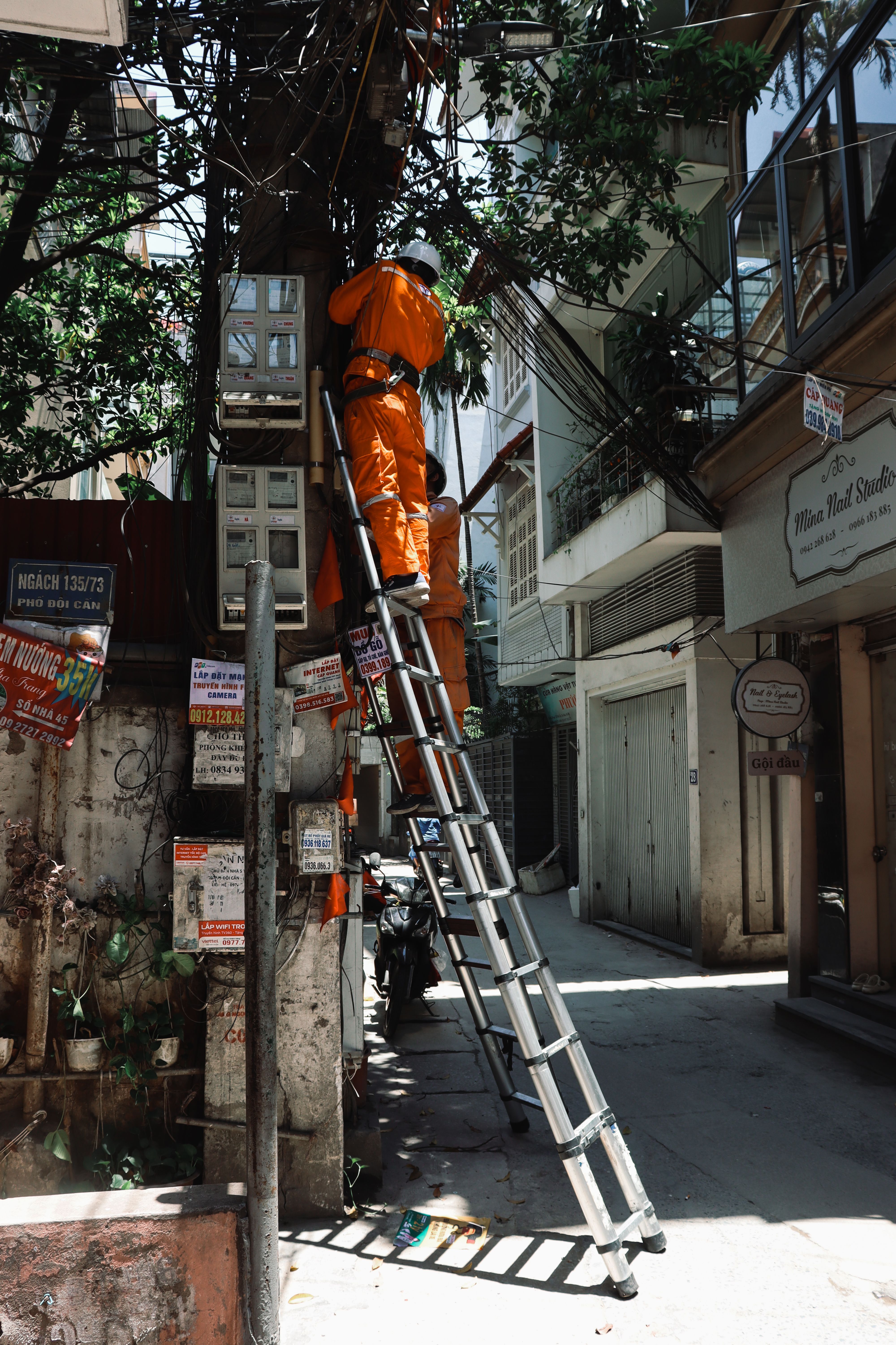 Electrician in orange uniform working on a power line in Hanoi street.