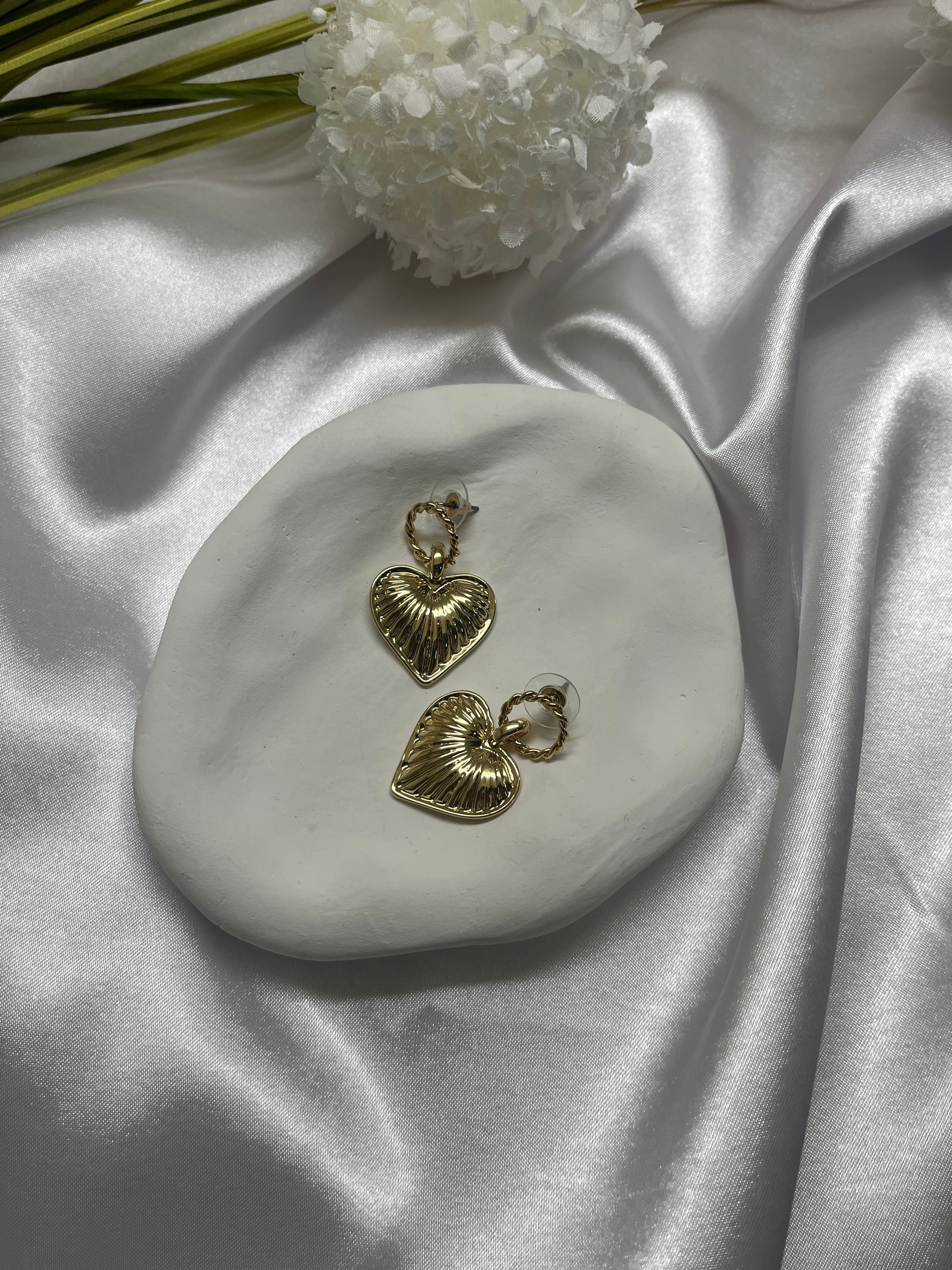 Beautiful heart-shaped golden earrings elegantly displayed on silky white fabric.
