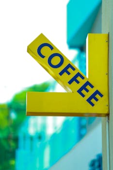 Vibrant yellow coffee sign hangs on building, directing towards a café. Urban appeal with bright colors.