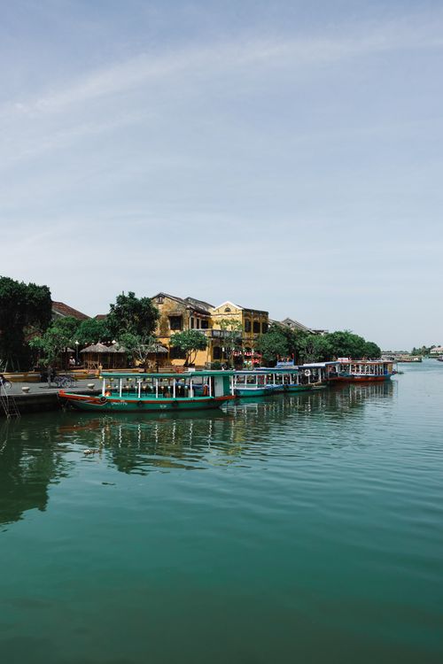 Free Colorful boats on a tranquil river in Hội An, showcasing Vietnamese architecture. Stock Photo