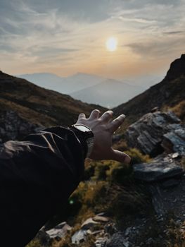 Hand reaching towards a sunset over rocky mountains in Erbil, Iraq.
