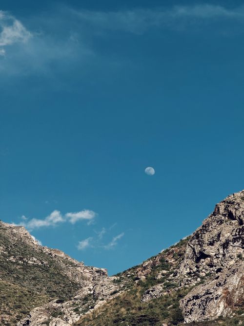 Free A serene view of Erbil's rugged mountains with a visible moon overhead against a bright blue sky. Stock Photo