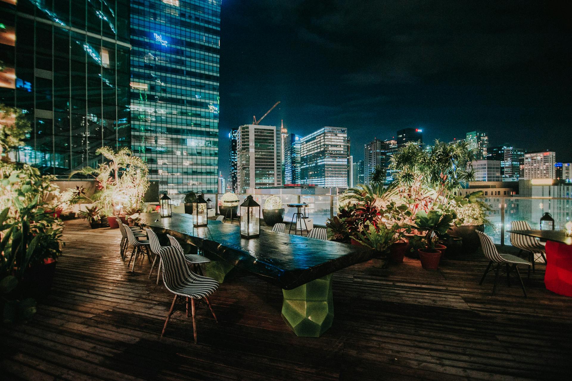 A vibrant rooftop garden with seating overlooking an illuminated cityscape at night.