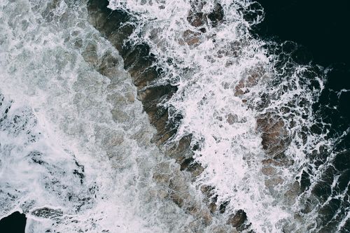 Free Captivating aerial shot of ocean waves crashing on a rugged seashore, showcasing nature's raw beauty. Stock Photo
